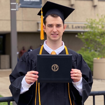 A portrait photo of Matthew Kosloski wearing graduation attire and holding his diploma